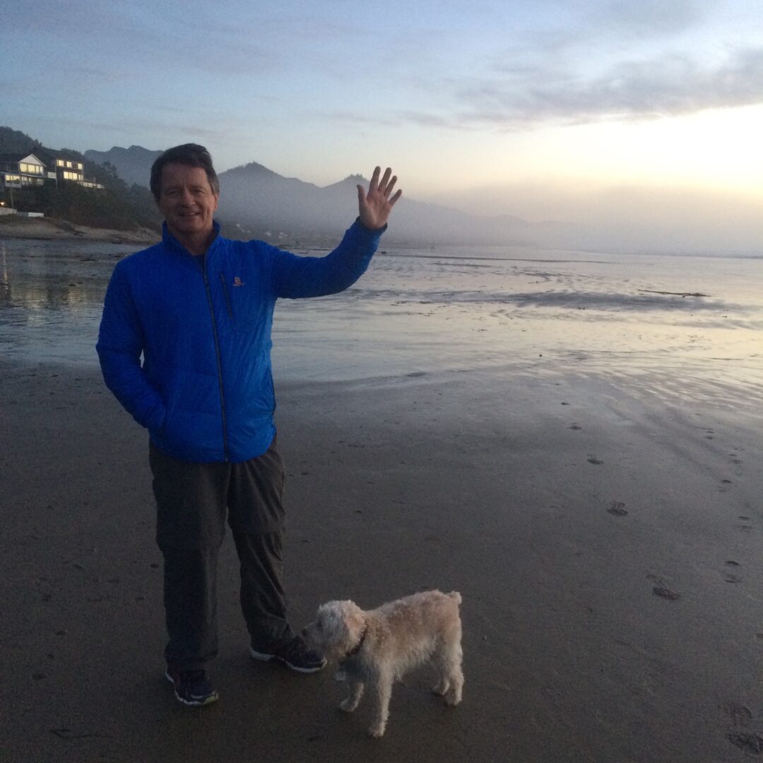 A man and his dog on the beach waving.