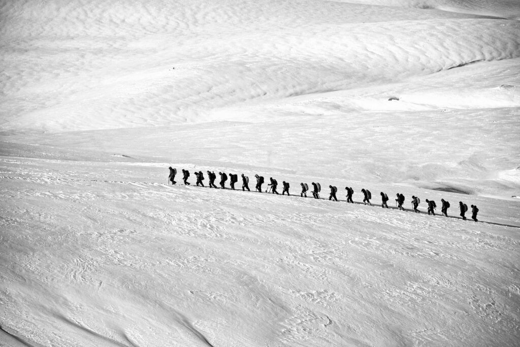 Hikers in a single file line on snowy mountain.